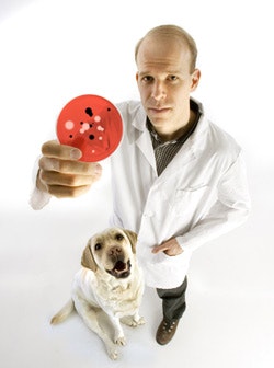 Scott Weese with a golden retreiver. Scott is holding up a palette with bacteria