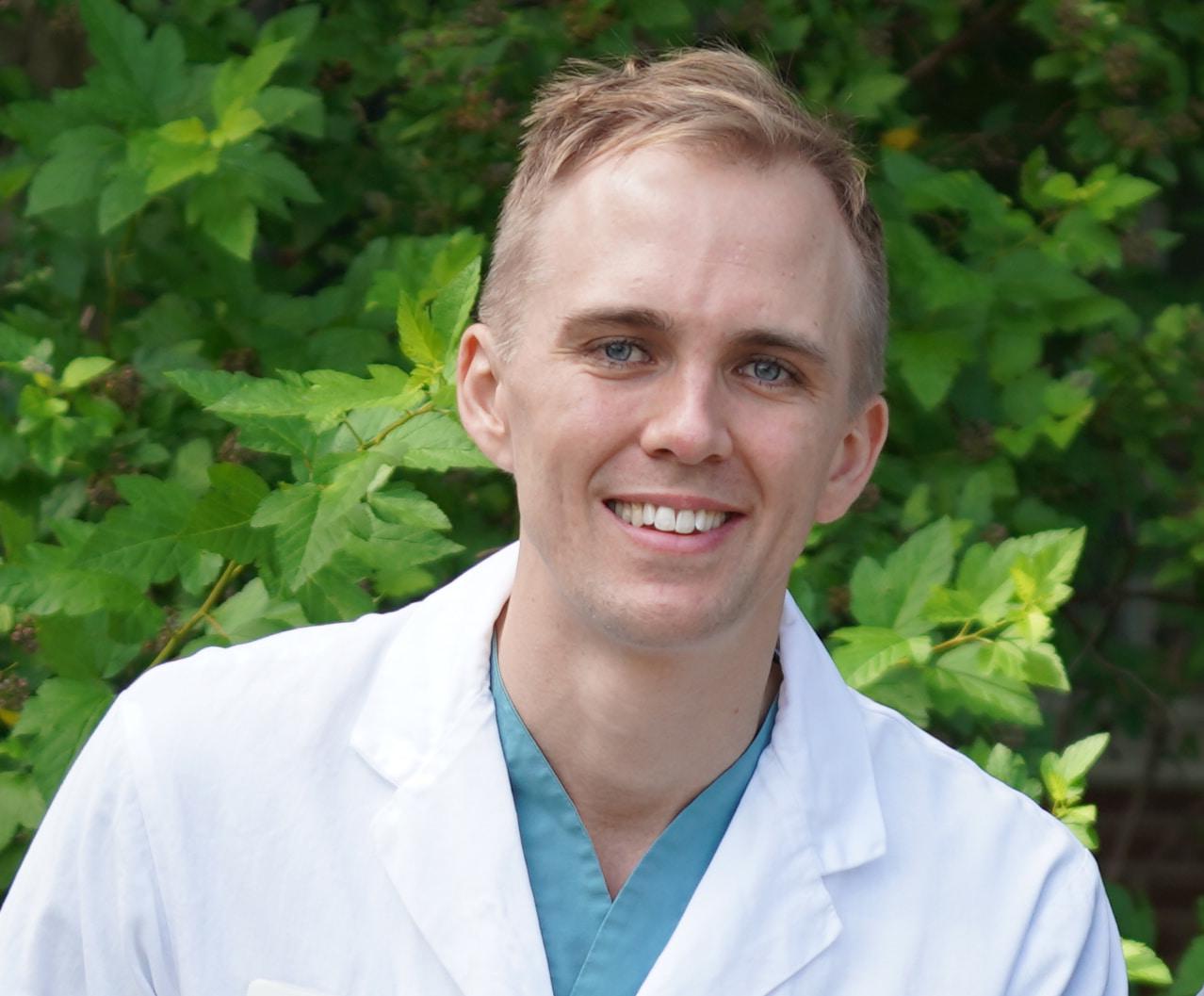 A man standing outside with blonde hair wearing a white lab coat